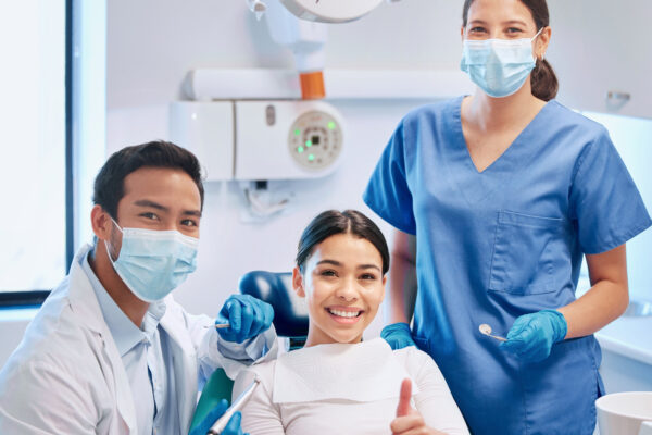 Shot of a young male dentist giving the thumbs up with his patient and assistant.