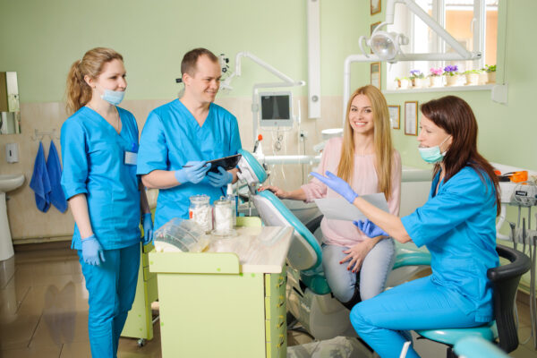 Young beautiful happy woman with three doctors at the dental office. Dental health. Oral procedure concept. Stomatology equipment