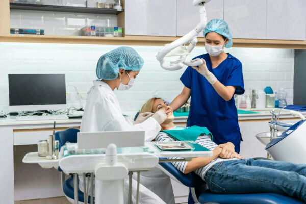 Female dentist examine tooth to Caucasian girl at dental health clinic. Attractive woman patient lying on dental chair get dental treatment from doctor during procedure appointment service in hospital